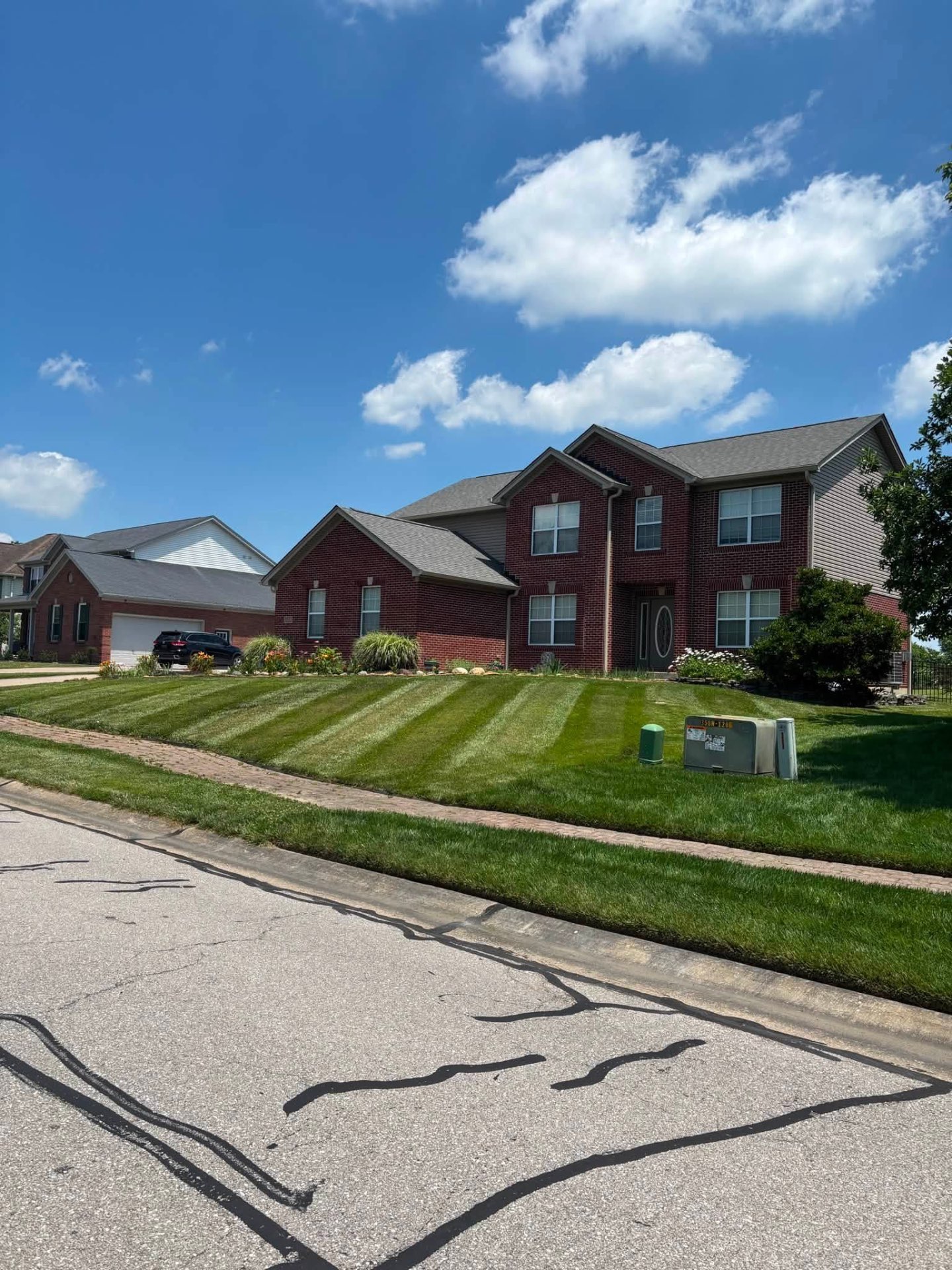 Two-story brick home with a hillside lawn cut in clean stripes
